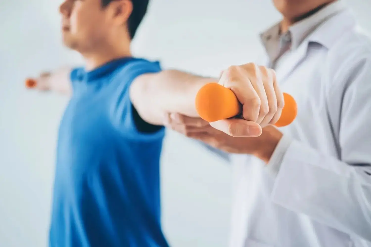 Physiotherapeut-Mann gibt Übung mit Hantelbehandlung über Arm und Schulter eines männlichen Athleten-Patienten Physiotherapie-Konzept