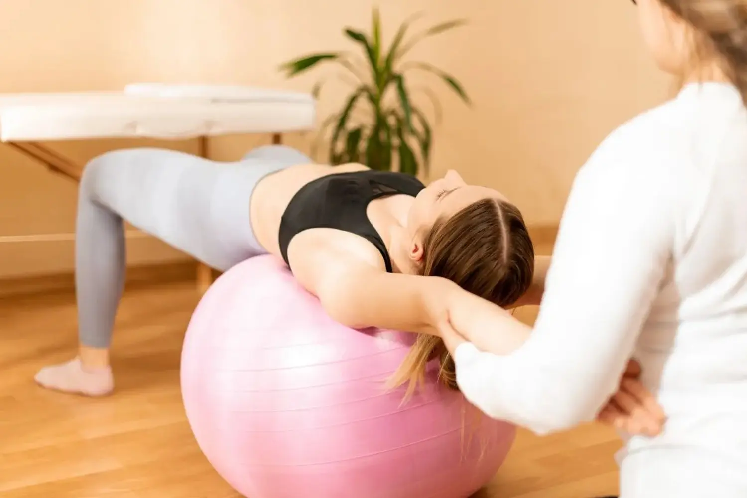 Physiotherapeutin arbeitet mit einer jungen Klientin an der Rumpfmuskulatur mittels Fitball. Hintergrund in Rehabilitation und Physiotherapie.