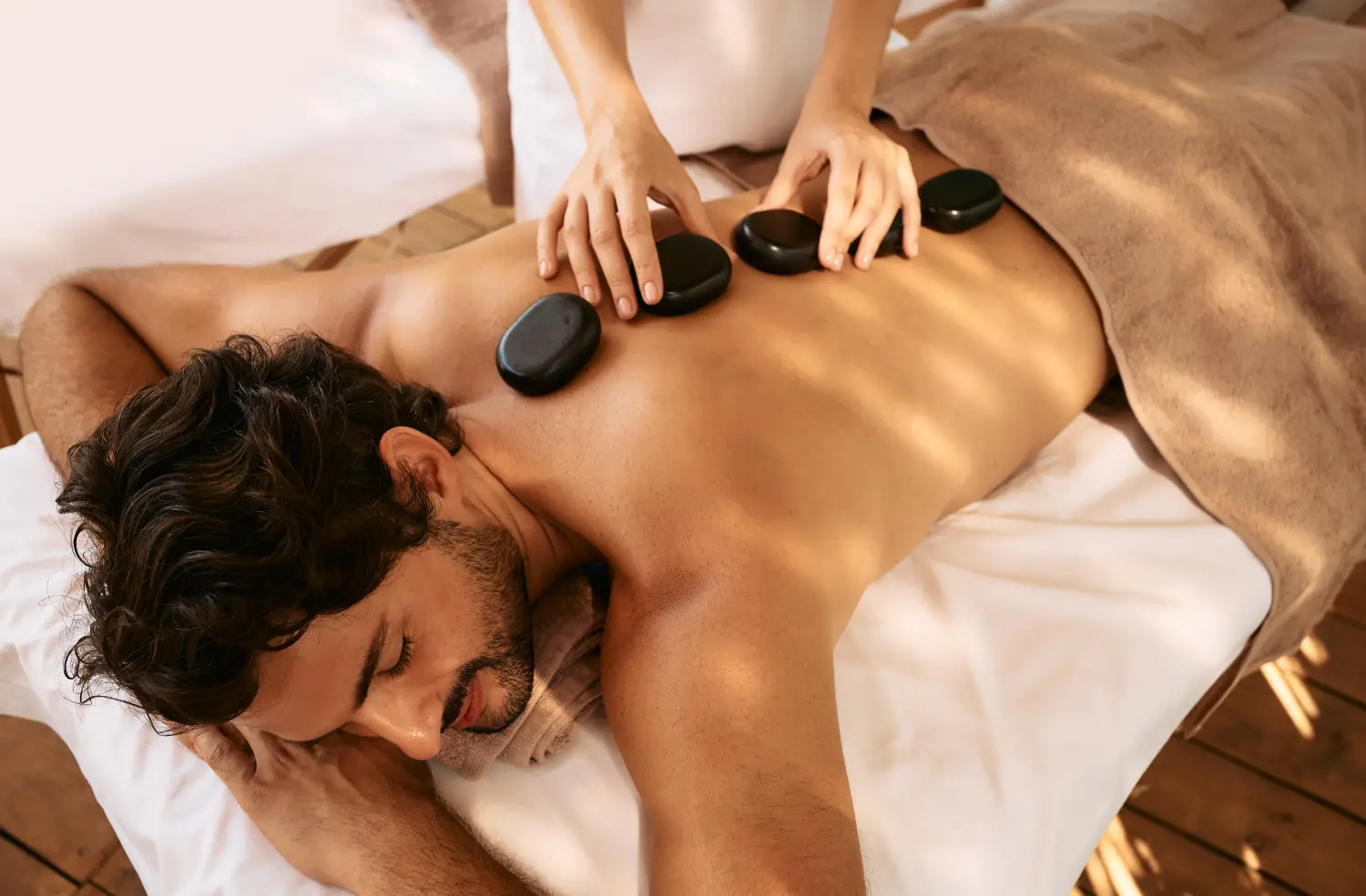 Schöner Mann im Spa-Resort erhält Hot-Stone-Massage. Hot-Stone-Massagetherapie mit glatten, flachen, erhitzten Steinen